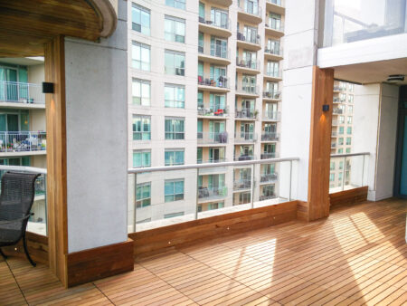 Modern apartment balcony with IPE wooden flooring, glass railing, and views of neighboring balconies.
