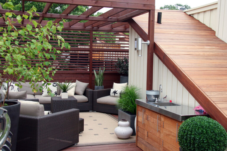 Rooftop patio with wicker seating, wood pergola, outdoor sink, potted plants, and a wooden staircase.