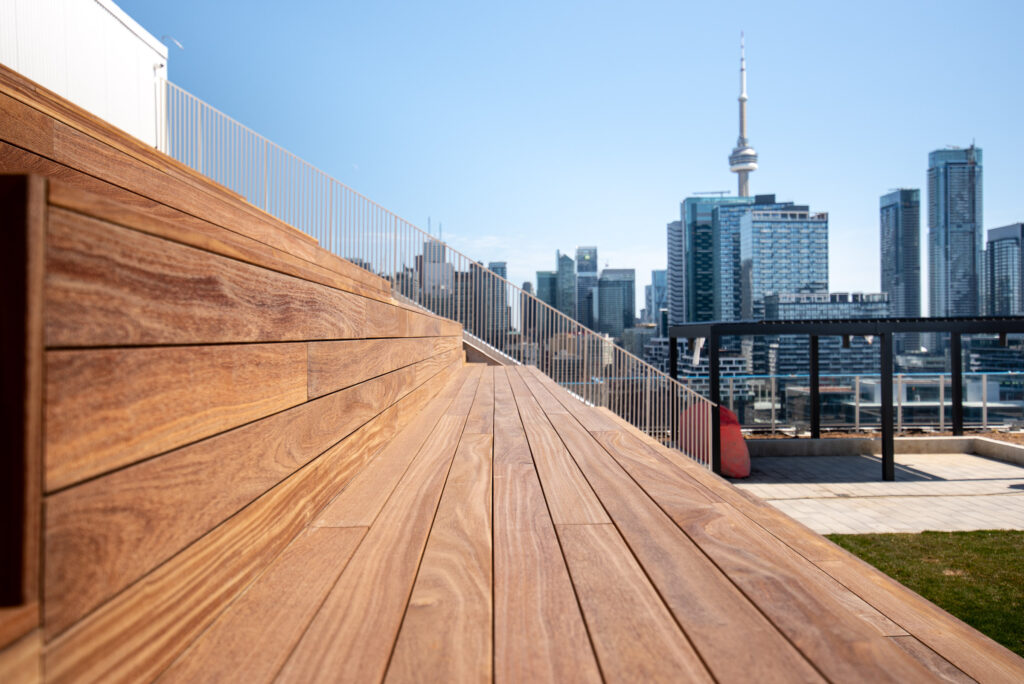 Wooden bleachers with a city skyline and tall tower in the background under a clear blue sky.