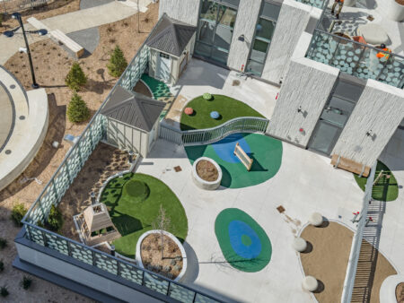Aerial view of a modern outdoor playground with artificial turf, benches, and play structures on a rooftop terrace.