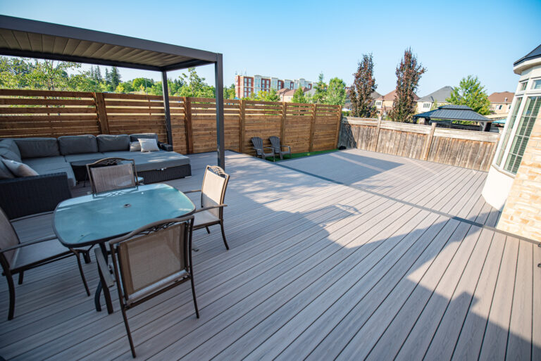 Spacious backyard deck with patio furniture, seating area under a canopy, and wooden privacy fence on a sunny day.
