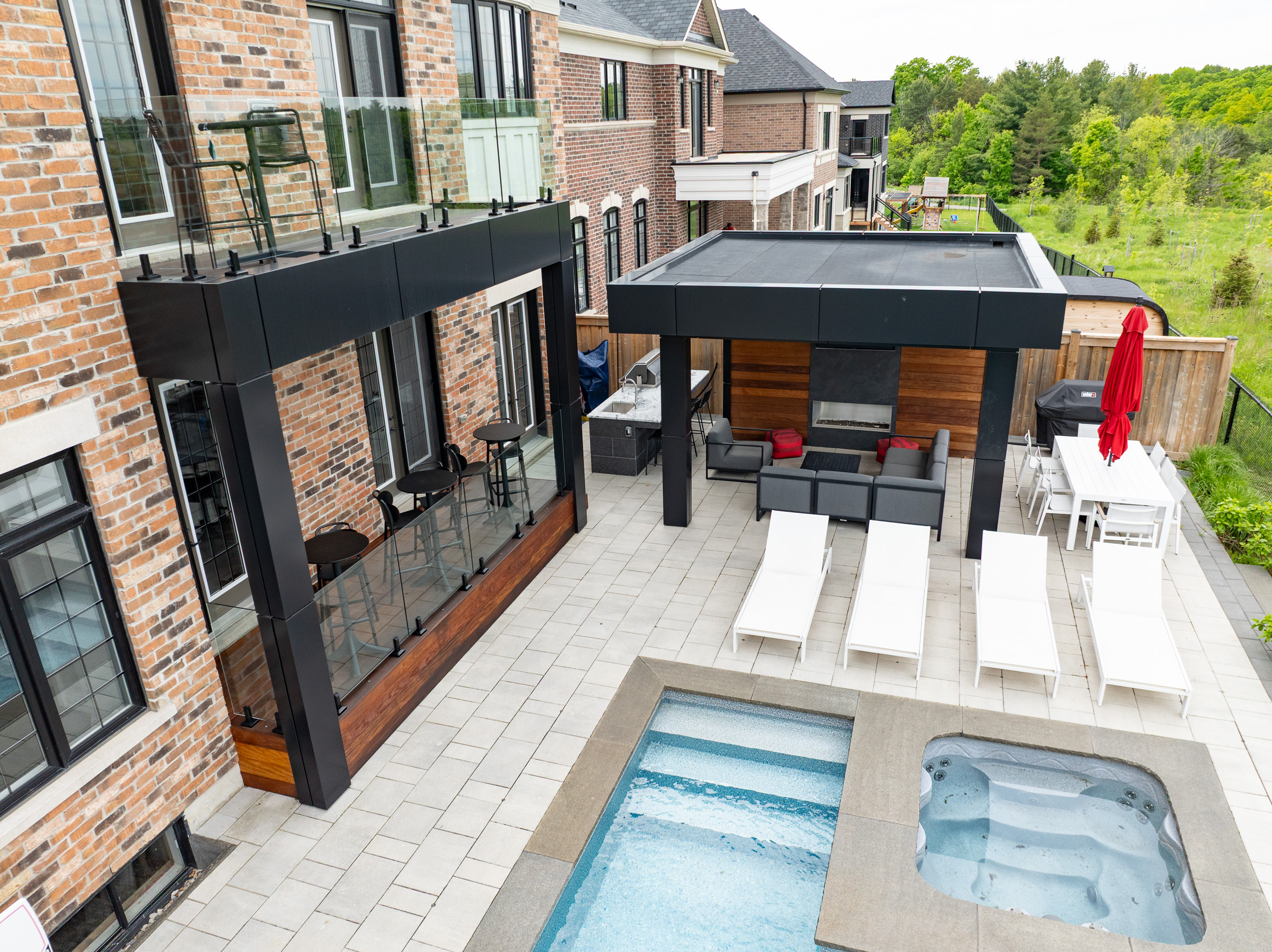 A modern backyard with a pool, hot tub, lounge chairs, patio seating area, and dining table with a red umbrella.