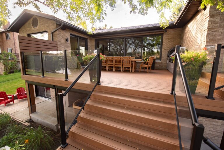 Raised wooden deck with glass railings, outdoor dining table, and stairs leading to a grassy backyard.