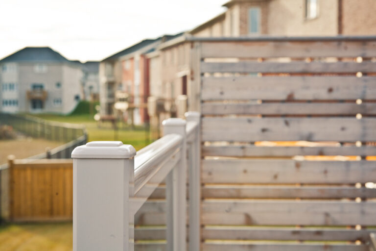 White railing and wooden privacy fence on a residential deck with suburban houses in the background.