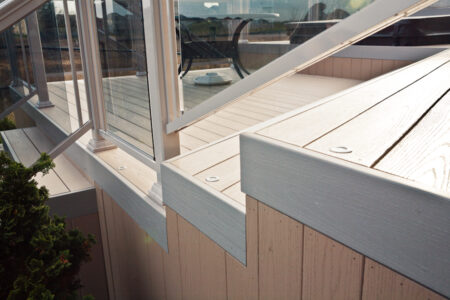 Close-up of a modern deck with light-colored wood, metal railing, and glass panels, seen in daylight.